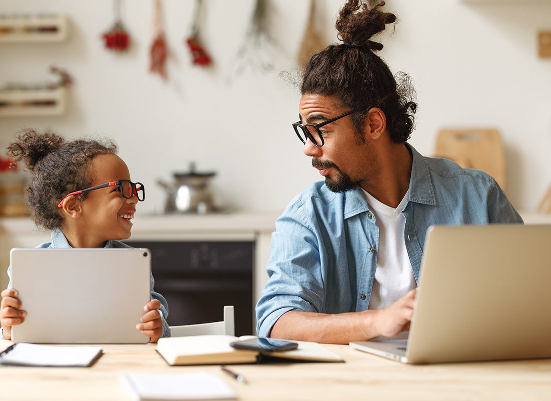 About Our Agency - Happy Father and Son Look at Each Other and Smile While They Use a Laptop and a Tablet