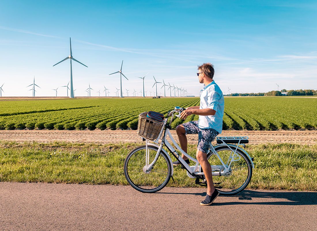Employee Benefits - Man on a Bike Takes a Break to Look at a Crop Field and Windmills on a Sunny Day
